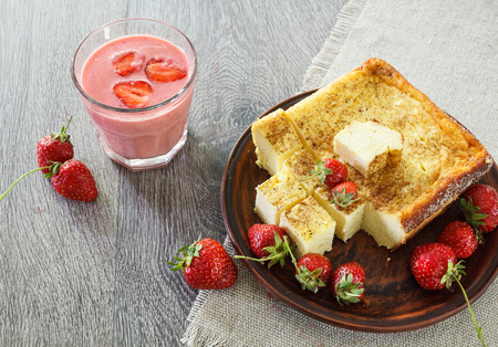 Glass of strawberry smoothie and cheesecake. On a wooden table strawberries and linen napkinの写真素材