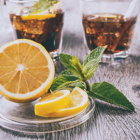 The cooling drink with ice, lemon and mint. Cola in glass on a wooden table.