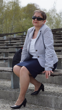 The woman in a blue skirt and black shoes is sitting on the bench and waiting for someoneの写真素材