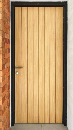 light-colored wooden door with vertical paneling and a black frame,set against a brick wall on one sideの写真素材