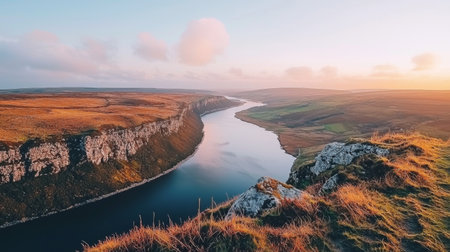 Discover a stunning river valley at sunset, featuring dramatic cliffs, golden grasslands, and a warm sky. A perfect escape into serene natural beauty and tranquility.の素材