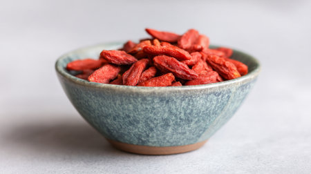 A close-up view of a bowl filled with vibrant goji berries, highlighting their bright red hue and inviting texture, perfect for health enthusiasts and culinary uses.の素材