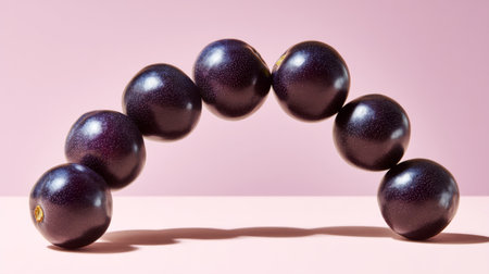 A unique composition of dark purple fruits creating an arch shape on a soft pink background, symbolizing freshness and nutrition in a modern, artistic style.の素材