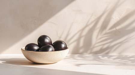 A serene arrangement of fresh black plums in a light bowl, casting soft shadows on a creamy surface, embodying a natural and healthy aesthetic perfect for food visuals.の素材
