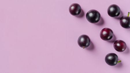This captivating image showcases fresh dark purple grapes arranged on a soft pink background, highlighting their vibrant color and natural beauty in a stylish and modern composition.の素材