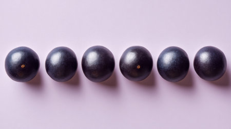 A stunning arrangement of six round dark purple fruit set against a soft pastel background, perfect for use in culinary and health-related projects and visuals.の素材