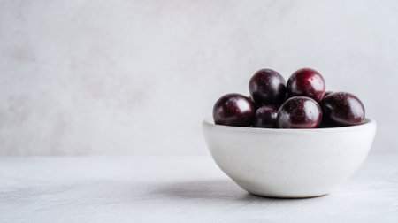 A minimalist composition featuring fresh, juicy plums in a round white bowl against a soft light background, ideal for healthy recipes, fruit inspiration, and culinary art.の素材