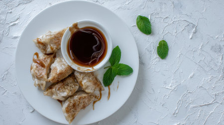 Enjoy a plate of delicious pan-fried dumplings paired with a savory dipping sauce and fresh mint leaves, perfect for any meal or snack time.の素材
