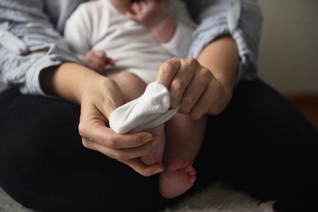 Young mother puts the socks on her little baby holding it in her armsの写真素材