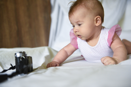 Little beautiful baby girl wondering looks at vintage film photo camera on a wooden wall background