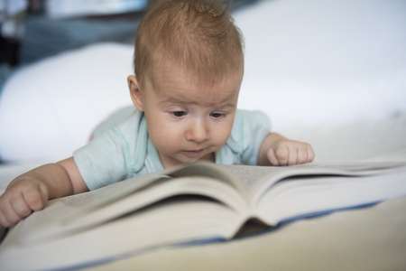 Portrait of cute baby girl lying over and trying to read a big bookの写真素材