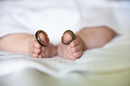 Feet of a newborn wearing his parents' wedding rings on his big toesの写真素材