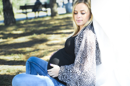 Beautiful pregnant woman poses holding her belly, in natureの写真素材