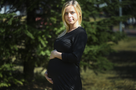 Beautiful pregnant woman poses holding her belly, in natureの写真素材