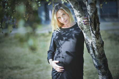 Beautiful pregnant woman poses holding her belly, in natureの写真素材