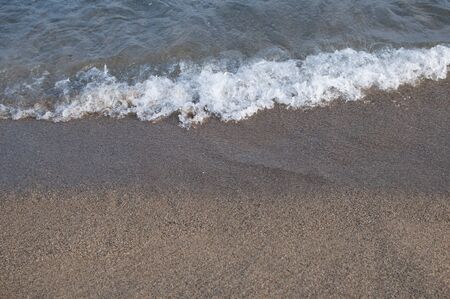 Coastline with the sand and waves on a sea sufrace and sky in background
