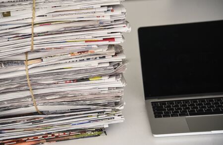 Pile of daily papers with news next to the computer.