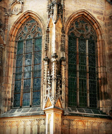 Close-up of a historical Gothic cathedral facade, showing two symmetrical arched windows with intricate stone tracery and dark stained glass. Ideal for themes of European history, grand architecture, religion, and travel destinations.の写真素材