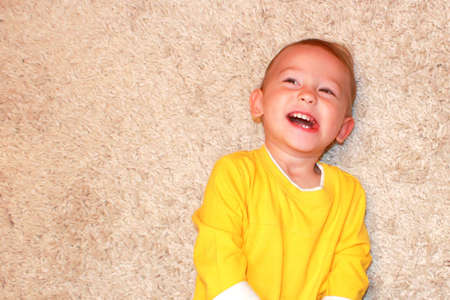 Portrait of a laughing baby lying on a carpet.の写真素材
