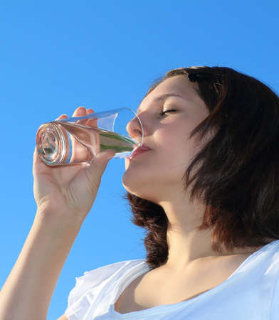 Young woman drinking water on sky backgroundの写真素材