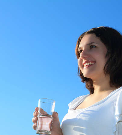 Young woman drinking water on sky backgroundの写真素材