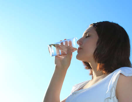 Young woman drinking water on sky backgroundの写真素材