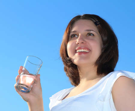 Young woman drinking water on sky backgroundの写真素材