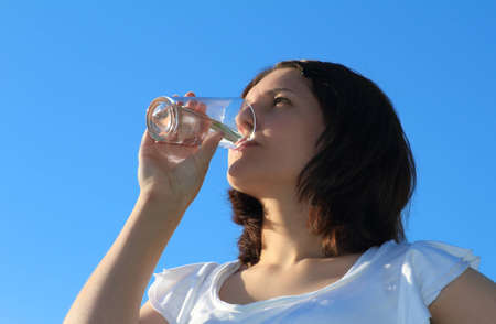 Young woman drinking water on sky backgroundの写真素材