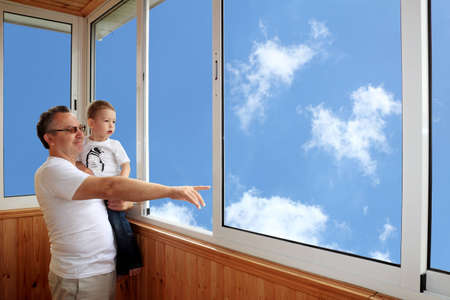 Grandson and grandfather standing on balcony and looking at the skyの写真素材