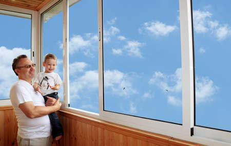 Grandson and grandfather standing on balcony and looking at the skyの写真素材