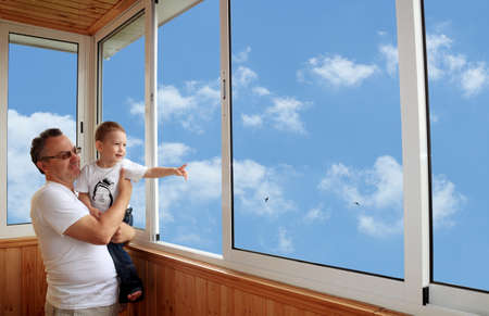 Grandson and grandfather standing on balcony and looking at the skyの写真素材