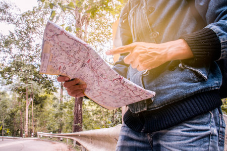 Asian traveler use of paper map to find their way,local highway and forest backgroundの写真素材