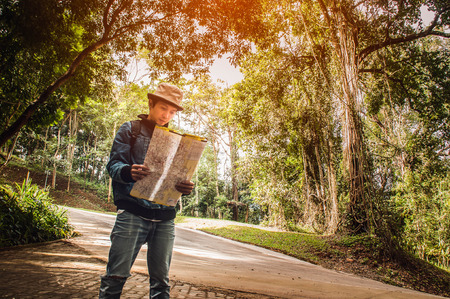 Asian traveler use of paper map to find their way,local highway and forest background