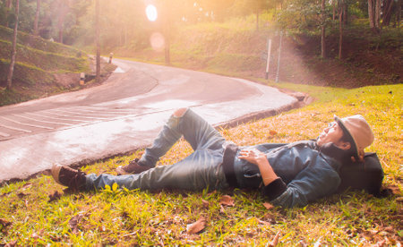 Happy man traveler lying on green lawn and relaxing at sunset timeの写真素材