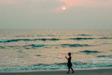 Silhouette of a girl walking along on the beach at sunsetの写真素材