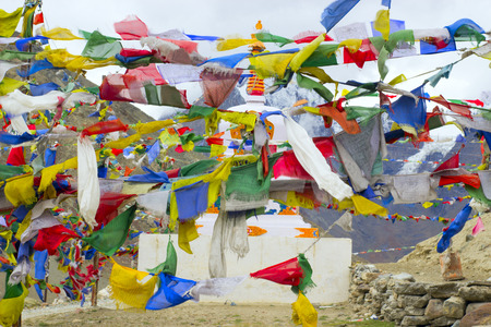 Tibetan multicolored flags surround a white stupa with an ornament in the mountains of the Himalayas.の写真素材