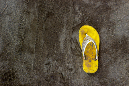 Only one dirty yellow sandal on the black sand. Horor concept.の写真素材