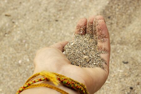 Sand from small shells in a womans hand with bracelets amulets on Kuta beach.の写真素材