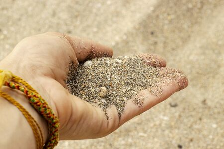 Sand from small crushed shells in a womans hand with bracelets amulets.の写真素材