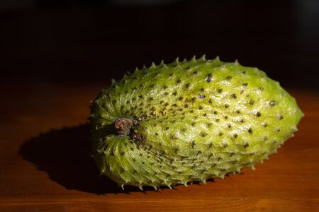 Green fruit Soursop on wooden table with dark background in sunlight.の写真素材