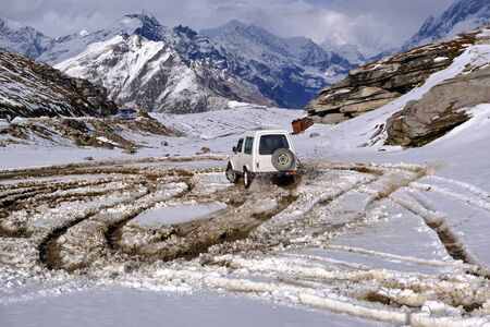 All-terrain vehicle with all-wheel drive drifting on freshly fallen snow high in the mountains of Himalayas near the track. The car creates circles on the snow with its movement. Snow flies beautifully from under the wheels. Can be used for rescueの写真素材