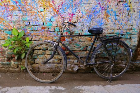A black old rusty Bicycle is parked against a green Bush and a colorful bright wall. The contrast of the new painting and the old thing next.の写真素材