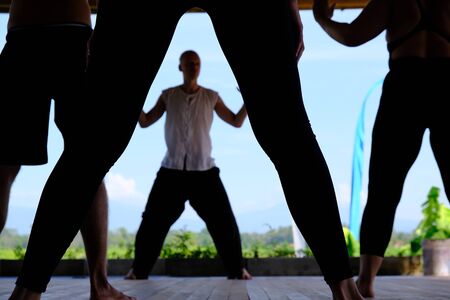 Several people practice qigong in the fresh air. Legs in the shadow and a man in the background. Healthy lifestyle and longevity practice.の写真素材