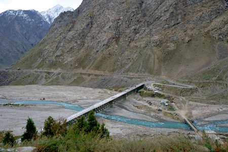 A bridge over a turquoise river in the vast snow-capped mountains of the Himalayasの写真素材