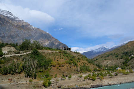 A building under construction on a hill among the mountains with snow-capped peaks near the riverの写真素材