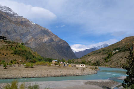 A cozy little village on the banks of a turquoise river in the mountains of the Himalayas on a clear autumn dayの写真素材