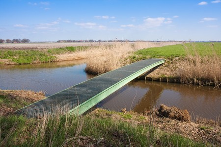 Dutch farmland with pedestrian bridge crossing a wide ditchの写真素材