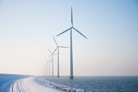 Long row of snowy windmills standing in Dutch sea disappearing in winter haze