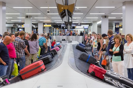 AMSTERDAM, THE NETHERLANDS - AUG 14: Airplane travelers are waiting for their luggage from a conveyor belt at Schiphol airport on August 14, 2014 in Amsterdam, The Netherlandsのeditorial素材
