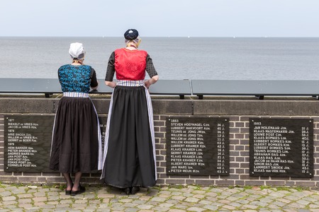 URK, THE NETHERLANDS - JUN 07: Two traditional dressed women from Urk visiting the monument of drown fishermen on June 07, 2014 at the coast of Urk, the Netherlandsのeditorial素材